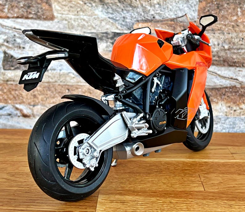 May include: Orange and black motorcycle model with the KTM logo on the side and tail. The motorcycle has a silver exhaust pipe and black wheels.