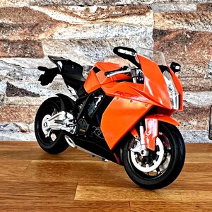 May include: Orange and black sport motorcycle with a black seat and a black windshield. The motorcycle is on a wooden floor in front of a brick wall.