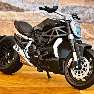 Peut inclure: Motocyclette noire avec un échappement argenté et des roues noires. La motocyclette est sur une surface en bois.