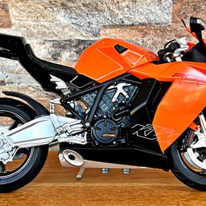 May include: A bright orange and black motorcycle with a sleek design. The motorcycle has a black seat and a black exhaust pipe. The motorcycle is on a wooden surface.
