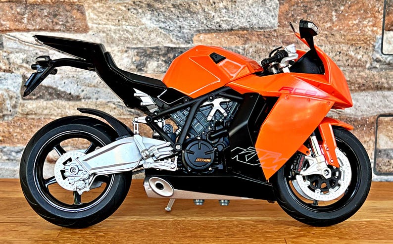 May include: A bright orange and black motorcycle with a sleek design. The motorcycle has a black seat and a black exhaust pipe. The motorcycle is on a wooden surface.
