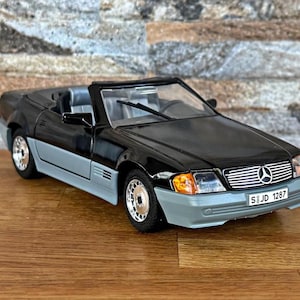 May include: A black and gray convertible model car with silver rims. The car has a Mercedes-Benz logo on the front and a license plate that reads SIJD 1287. The car is on a wooden surface.