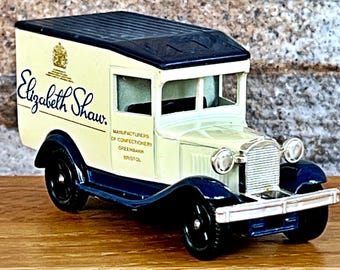 May include: A vintage toy delivery truck with a white body, blue trim, and a black roof. The truck has a sign that reads "Elizabeth Shaw. Manufacturers of Confectionery, Greenbank, Bristol."