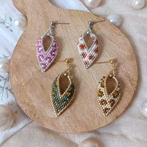 Peut inclure: Trois paires de boucles d'oreilles pendantes en forme de larme. Les boucles d'oreilles sont faites de petites perles dans une variété de motifs. Les motifs comprennent le rose et le blanc, l'orange et le blanc, et le vert et l'or.