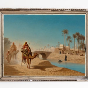 May include: A painting depicting a desert scene with a camel caravan traveling across a bridge over a river. The sky is blue and the sand is a warm brown. Palm trees line the riverbank and there are buildings in the distance.