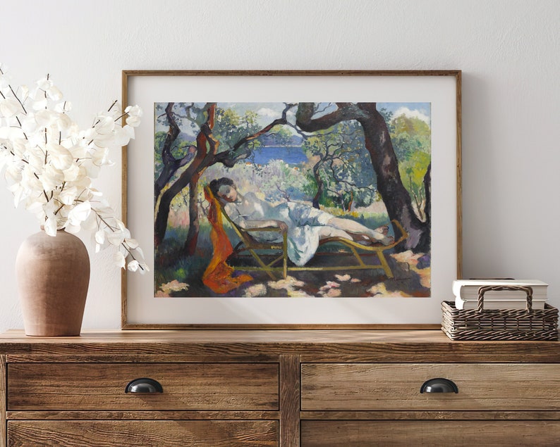 May include: A framed painting of a woman reclining on a chaise lounge in a garden setting. The woman is wearing a white dress and a red scarf. The garden is filled with trees and flowers. The painting is done in a style reminiscent of Impressionism.