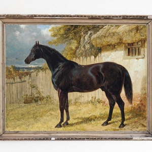 May include: A painting of a black horse standing in a field near a stone building with a thatched roof. The horse is facing to the left and has a long tail. The painting is framed in a wooden frame.