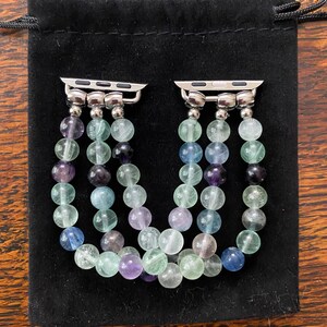 K&ouml;nnte beinhalten: Zwei silberne Armb&auml;nder mit drei Str&auml;ngen bunter Edelsteinperlen. Die Perlen sind eine Mischung aus Hellgr&uuml;n, Blau und Lila.