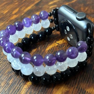 May include: A black, white, and purple beaded Apple Watch band. The band is made of amethyst, clear quartz, and black onyx beads.
