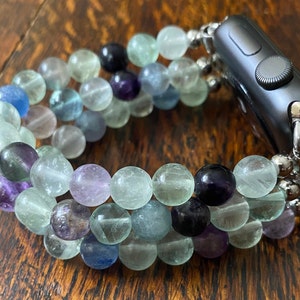 K&ouml;nnte beinhalten: Ein mehrfarbiges Perlenarmband f&uuml;r die Apple Watch mit gr&uuml;nen, blauen und violetten Perlen. Das Armband besteht aus nat&uuml;rlichen Steinen und ist f&uuml;r eine Standard-Apple Watch konzipiert.