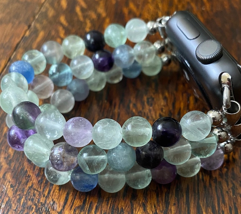 K&ouml;nnte beinhalten: Ein mehrfarbiges Perlenarmband f&uuml;r die Apple Watch mit gr&uuml;nen, blauen und violetten Perlen. Das Armband besteht aus nat&uuml;rlichen Steinen und ist f&uuml;r eine Standard-Apple Watch konzipiert.