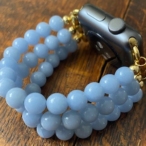 May include: A light blue beaded bracelet with a gold clasp, designed to fit an Apple Watch.