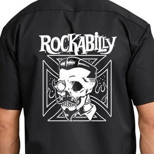 May include: Black short-sleeved work shirt with a white graphic of a skull with a mustache and glasses, wearing a bow tie. The graphic is inside a white cross with the word "Rockabilly" above it.