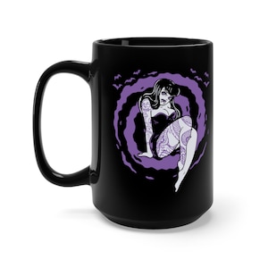 K&ouml;nnte beinhalten: Schwarze Keramiktasse mit einer lilafarbenen Illustration einer Frau mit einem Schlangentattoo, die in einer Wolke aus Flederm&auml;usen sitzt.