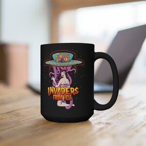 May include: Black ceramic mug with a graphic of a woman in a bikini being abducted by an alien spaceship with the text "INVADERS FROM HELL".