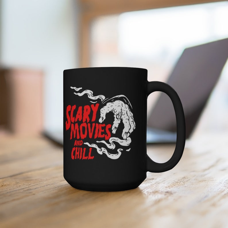 Peut inclure: Mug &agrave; caf&eacute; noir avec un graphique blanc d'une main sortant de la fum&eacute;e avec le texte "Scary Movies and Chill" en rouge.