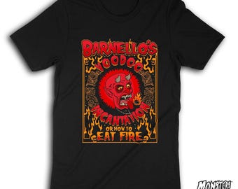 Peut inclure: Un t-shirt noir à manches courtes avec une impression graphique représentant un visage de diable rouge avec des cornes et des dents pointues. Le texte indique : BARNELLO'S VOODOO INCANTATION OR HOW TO EAT FIRE. Le motif inclut des flammes orange.