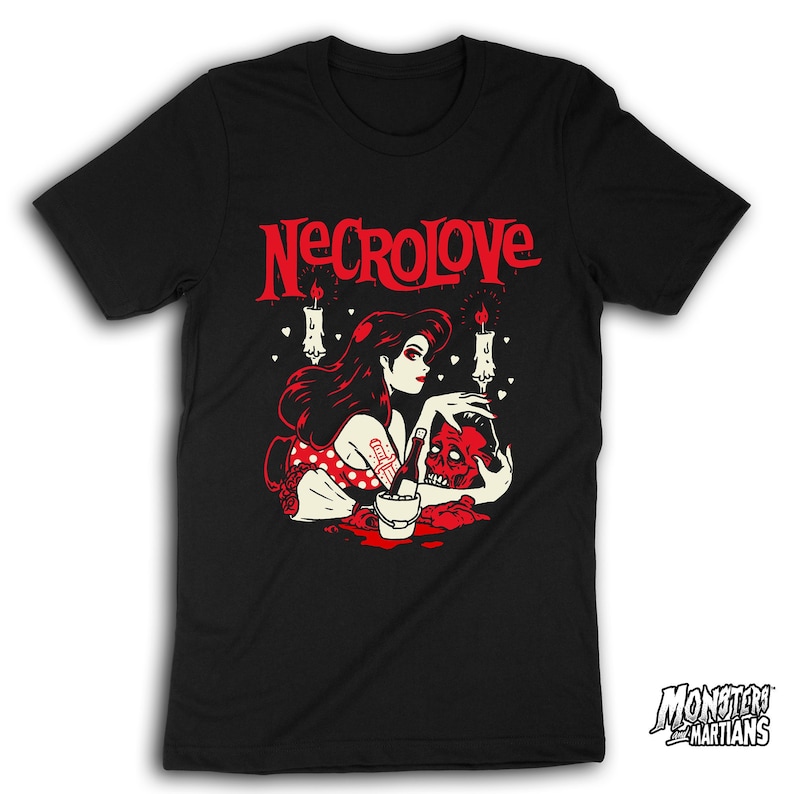 Puede incluir: Camiseta negra con un gr&aacute;fico rojo de una mujer con cabello negro largo sosteniendo una calavera. El gr&aacute;fico tambi&eacute;n incluye velas y corazones. El texto "NECROLOVE" est&aacute; impreso en rojo sobre el gr&aacute;fico.