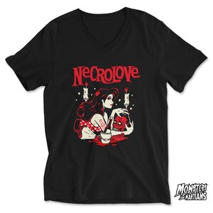 Puede incluir: Camiseta negra de cuello en V con un gr&aacute;fico rojo de una mujer con cabello negro largo sosteniendo una calavera. El gr&aacute;fico tambi&eacute;n incluye velas y corazones. El texto "NECROLOVE" est&aacute; impreso en rojo sobre el gr&aacute;fico.