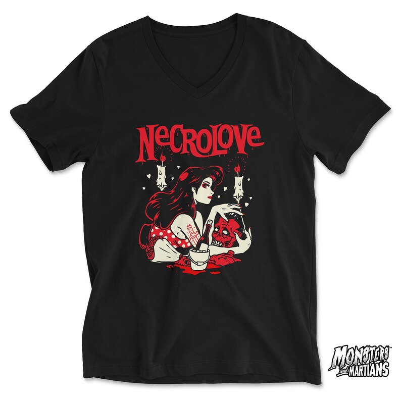 Puede incluir: Camiseta negra de cuello en V con un gr&aacute;fico rojo de una mujer con cabello negro largo sosteniendo una calavera. El gr&aacute;fico tambi&eacute;n incluye velas y corazones. El texto "NECROLOVE" est&aacute; impreso en rojo sobre el gr&aacute;fico.