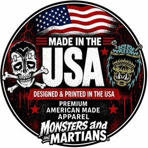 a circular logo with a skull and crossbones design, an American flag, and a monster or alien head. The text "MADE IN THE USA" is prominently displayed, along with the phrase "DESIGNED & PRINTED IN THE USA" and "PREMIUM AMERICAN MADE APPAREL" below. The phrase "MONSTERS and MARIANTS" is also included in the design.