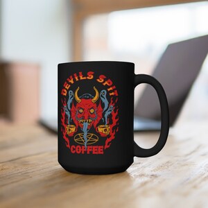 以下が含まれることがあります： 炎に囲まれた赤い悪魔の顔と「Devils Spit Coffee」の文字が書かれた黒いコーヒーカップです。