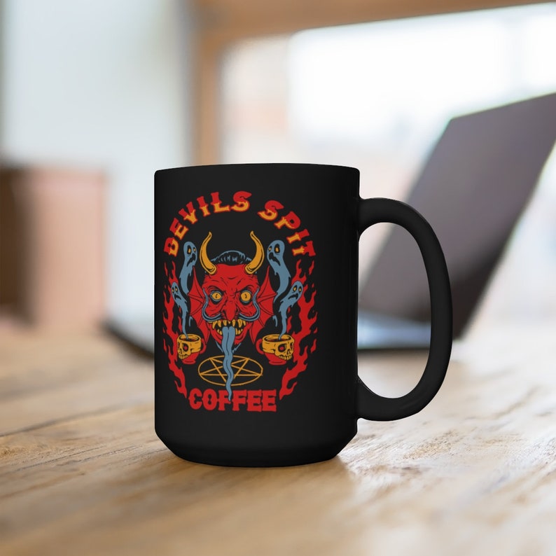 以下が含まれることがあります： 炎に囲まれた赤い悪魔の顔と「Devils Spit Coffee」の文字が書かれた黒いコーヒーカップです。