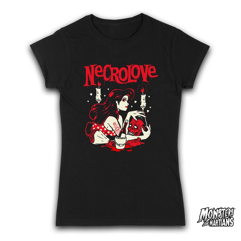 Puede incluir: Camiseta negra con un gr&aacute;fico rojo de una mujer con el pelo largo y negro sosteniendo una calavera. El gr&aacute;fico tambi&eacute;n incluye velas y corazones. El texto "NECROLOVE" est&aacute; impreso en rojo sobre el gr&aacute;fico.