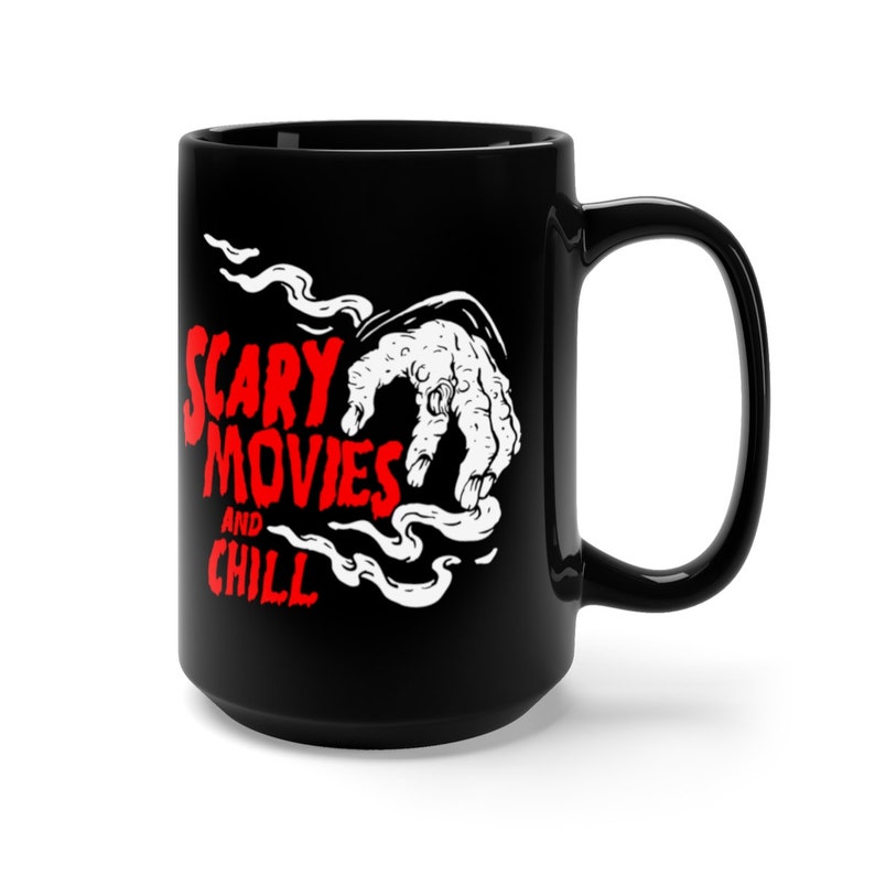 Peut inclure: Une tasse en c&eacute;ramique noire avec un graphique blanc d'une main sortant de la fum&eacute;e avec le texte "Scary Movies and Chill" en rouge.