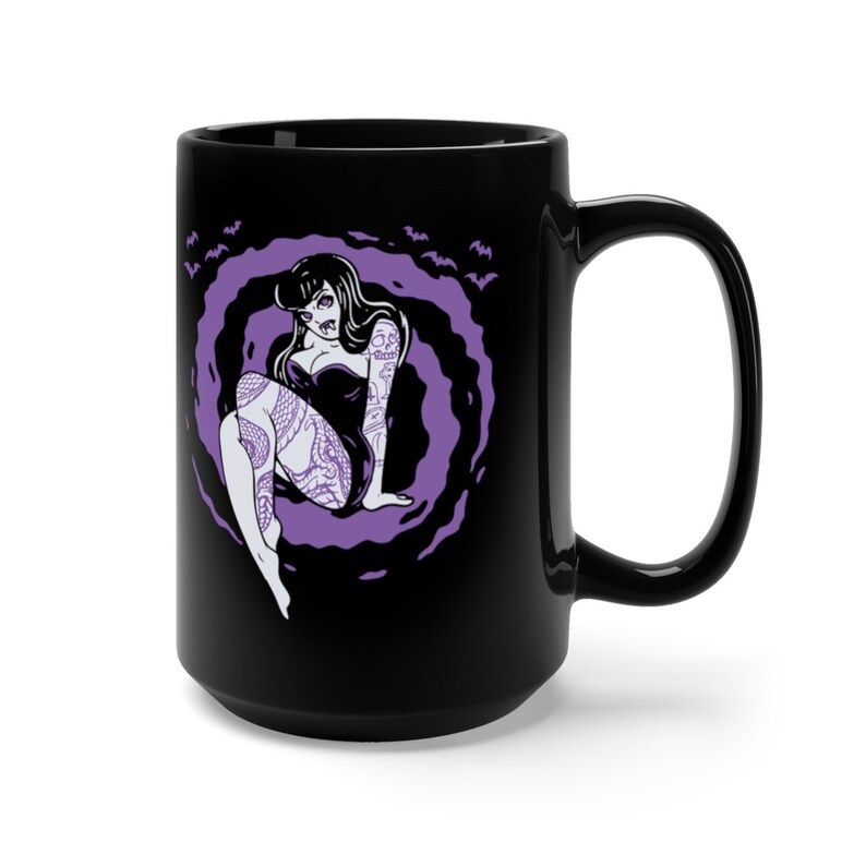 K&ouml;nnte beinhalten: Schwarze Keramiktasse mit einer lilafarbenen Illustration einer t&auml;towierten Frau, die in einer wirbelnden Wolke sitzt. Flederm&auml;use fliegen um die Wolke herum.