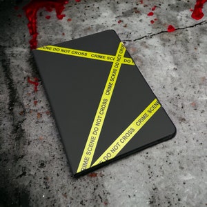 May include: A black notebook with yellow crime scene tape wrapped around it. The tape reads "Crime Scene Do Not Cross".
