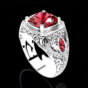 Könnte beinhalten: Silberner Ring mit einem großen, quadratisch geschliffenen roten Edelstein. Der Ring hat aufwendige Filigranarbeiten, kleine Diamanten und einen tropfenförmigen roten Stein an der Seite. Der Hintergrund ist schwarz.
