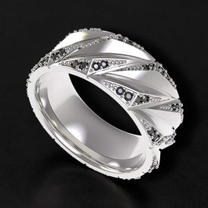 Könnte beinhalten: Ein silberner Ring mit geometrischem Design, der dreieckige Facetten und kleine schwarze Edelsteine aufweist. Der Ring hat eine polierte Oberfläche und ist vor einem dunklen Hintergrund platziert, der seine komplizierten Details hervorhebt.