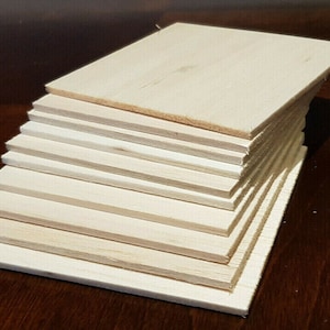 May include: A stack of 10 unfinished wood squares, each measuring approximately 15 cm by 15 cm. The wood is light brown and has a smooth surface.