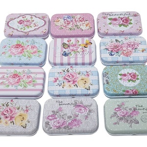 May include: Twelve small, rectangular, metal tins with floral designs. The tins have a white background with various floral patterns in pink, blue, and green. Some tins have text that reads "The beautiful garden".