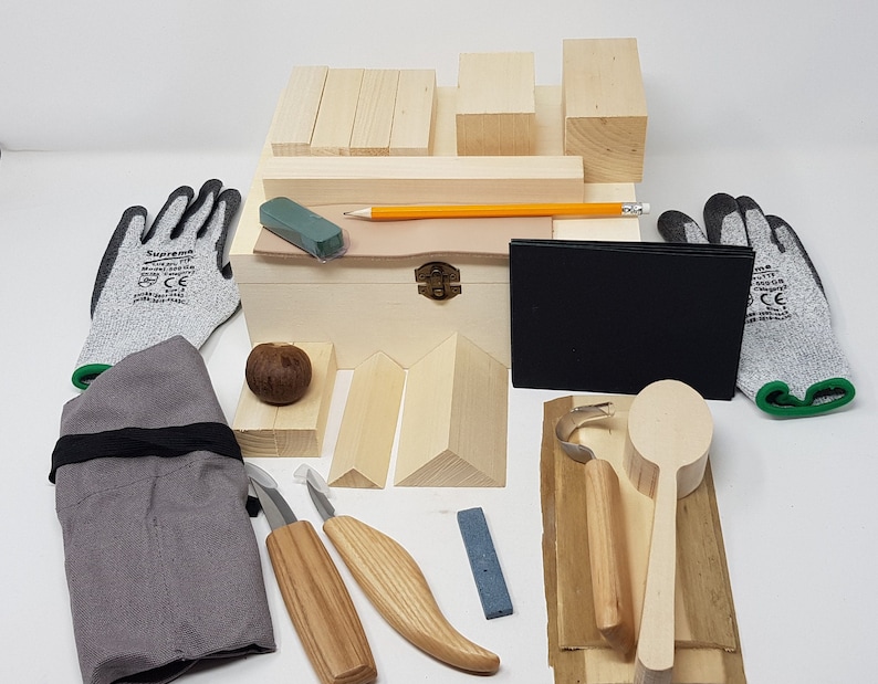 May include: A wood carving kit containing a wooden box, carving tools, wood blanks, a sharpening stone, gloves, and a pencil. The box is made of light wood and has a brass latch. The carving tools are made of wood and metal. The wood blanks are of various shapes and sizes. The sharpening stone is grey and rectangular. The gloves are grey and have green accents. The pencil is yellow. The kit is ideal for beginners or experienced wood carvers.
