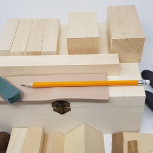 May include: A wooden box filled with various sized wooden blocks, a pencil, a green eraser, and a piece of leather. Two grey work gloves are on either side of the box.