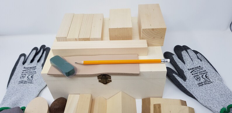 May include: A wooden box filled with various sized wooden blocks, a pencil, a green eraser, and a piece of leather. Two grey work gloves are on either side of the box.