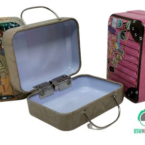 Könnte beinhalten: Drei kleine Vintage-Koffer mit Metallgriffen. Ein Koffer ist braun mit einem Route 66-Design, ein anderer ist pink mit Reiseaufklebern und der dritte ist grau mit einem hellblauen Innenraum.