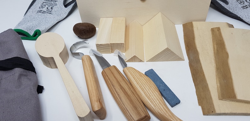 May include: Wood carving tools and supplies kit with a wooden spoon, three carving knives, a sharpening stone, and various wood blocks for practice.
