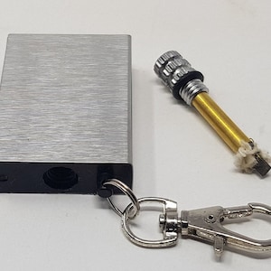 May include: A silver metal keychain lighter with a black plastic base and a silver metal key ring. The lighter has a small, round, silver metal striker on the side. The lighter is attached to a silver metal key ring.