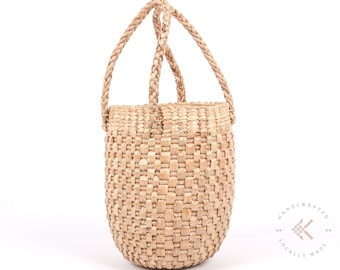 May include: A natural woven straw tote bag with two braided handles. The bag is a light beige colour and has a woven pattern. The bag is handcrafted and locally made.