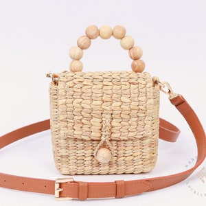 May include: A small, woven straw handbag with a brown leather strap and a wooden bead handle. The bag has a flap closure with a tassel.