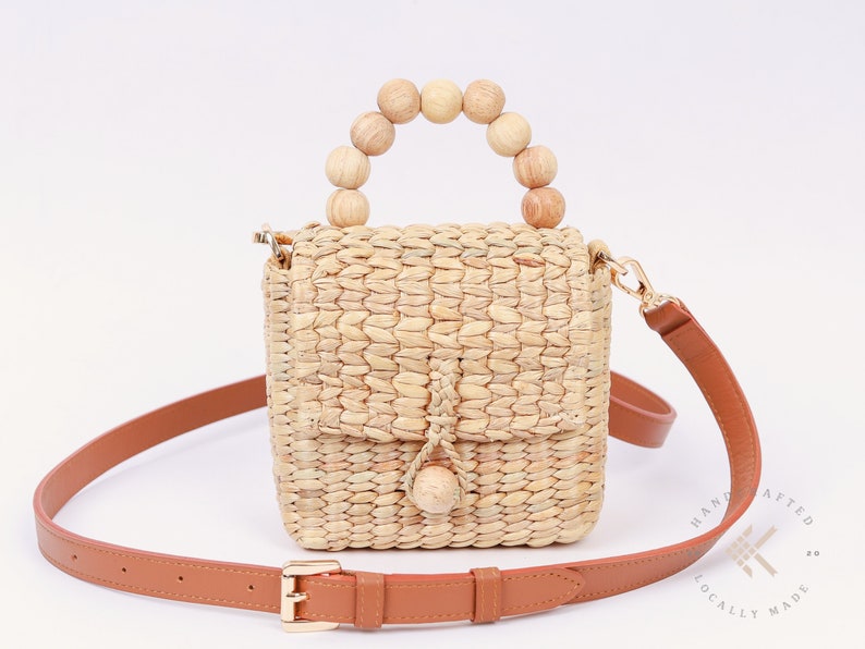 May include: A small, woven straw handbag with a brown leather strap and a wooden bead handle. The bag has a flap closure with a tassel.