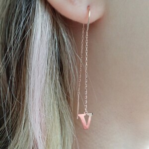 May include: Rose gold initial letter V dangle earrings. The earrings feature a delicate chain with a small letter V charm at the end.