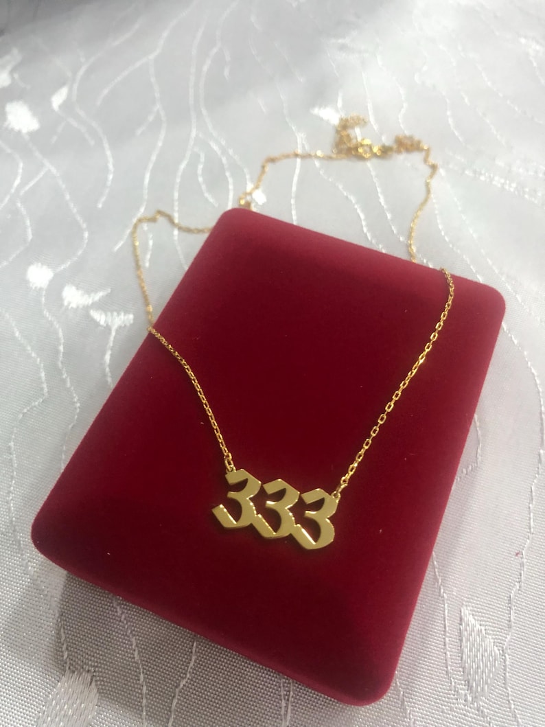 Op de afbeelding: Gouden ketting met een 333 hanger in een rode fluwelen doos.