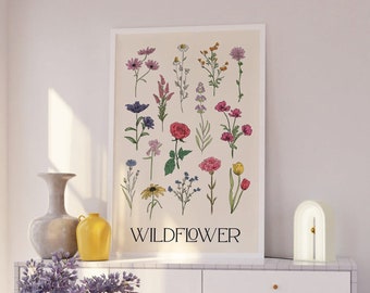Könnte beinhalten: Eine weiße Kommode mit drei Schubladen und goldenen Knöpfen. Eine weiße Lampe mit goldener Akzent steht auf der Kommode. Ein gerahmter Druck mit dem Wort "WILD FLOWER" und einer botanischen Illustration von Blumen hängt an der Wand hinter der Kommode. Eine Vase mit lila Blumen steht auf einem rosa Teppich vor der Kommode.
