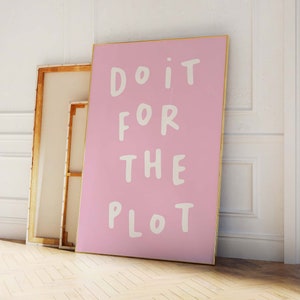 May include: A pink canvas print with a gold frame. The print features white text that reads "Do it for the plot."