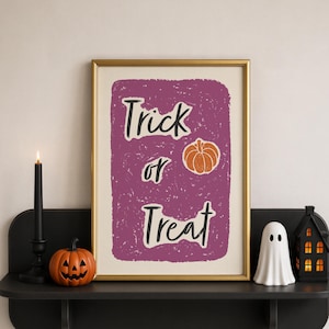 Può includere: Una stampa artistica incorniciata con uno sfondo viola testurizzato, il testo Trick or Treat in un carattere nero scritto a mano e una piccola illustrazione di una zucca arancione. La stampa è esposta in una cornice dorata su una mensola nera.