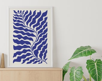 May include: A framed art print featuring a blue abstract botanical design on a cream background. The artwork is displayed in a white frame and rests on a light wood cabinet. A white vase and a potted plant with large green leaves are also visible.